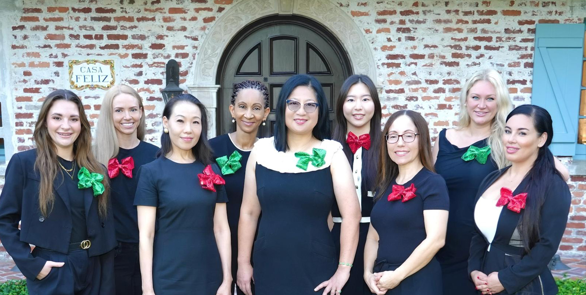 A group of individuals wearing black outfits with red bows on their ears, posing for a photo together in front of a brick building.
