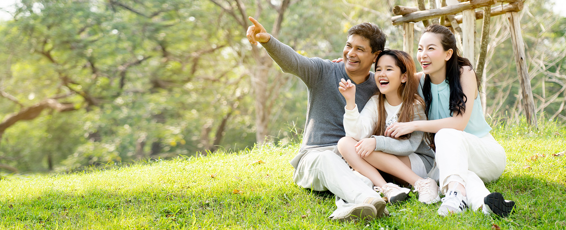 A family posing outdoors with a backdrop of trees and sky.