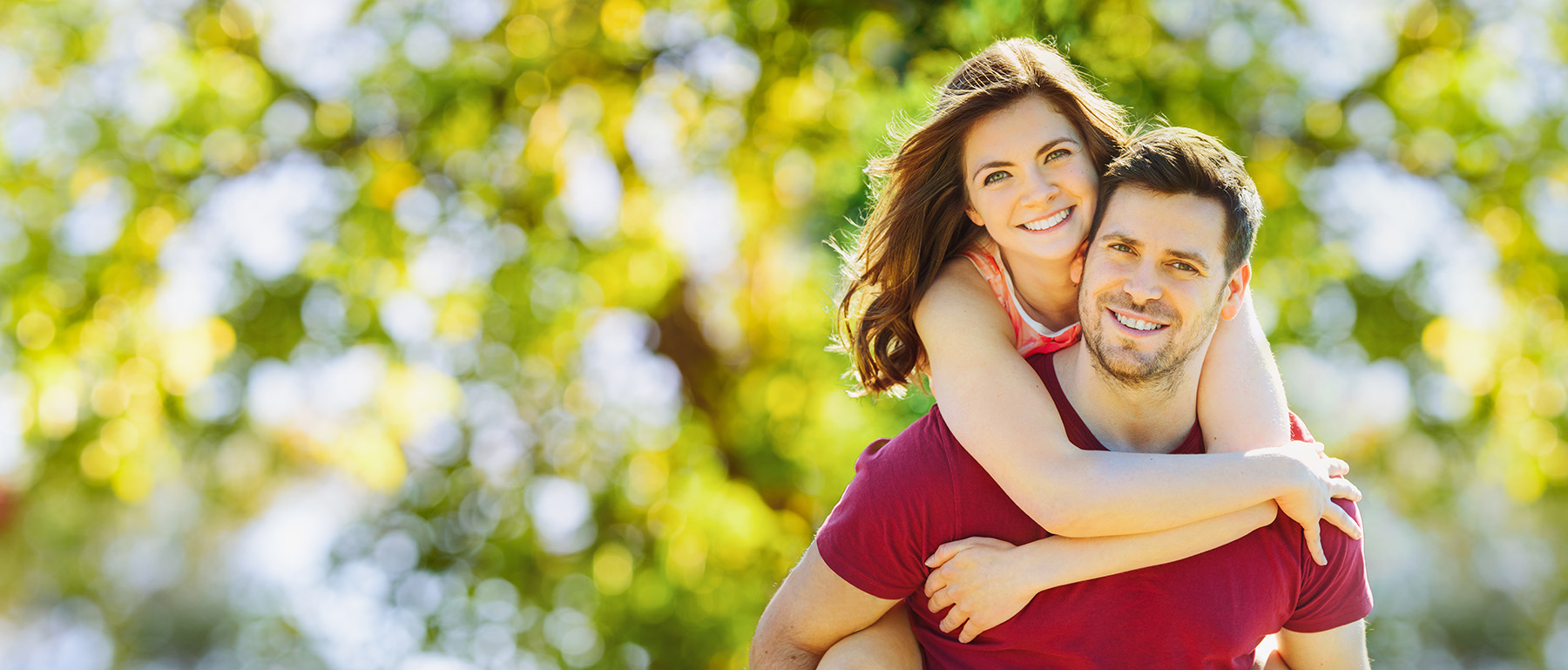 The image depicts a man and woman embracing each other outdoors with trees in the background.