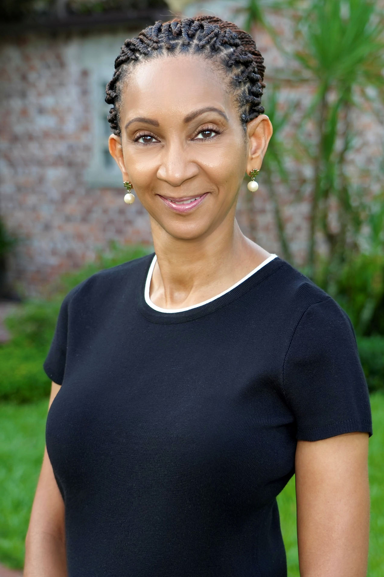A woman with a warm smile stands confidently against a backdrop of greenery, exuding an air of professionalism.